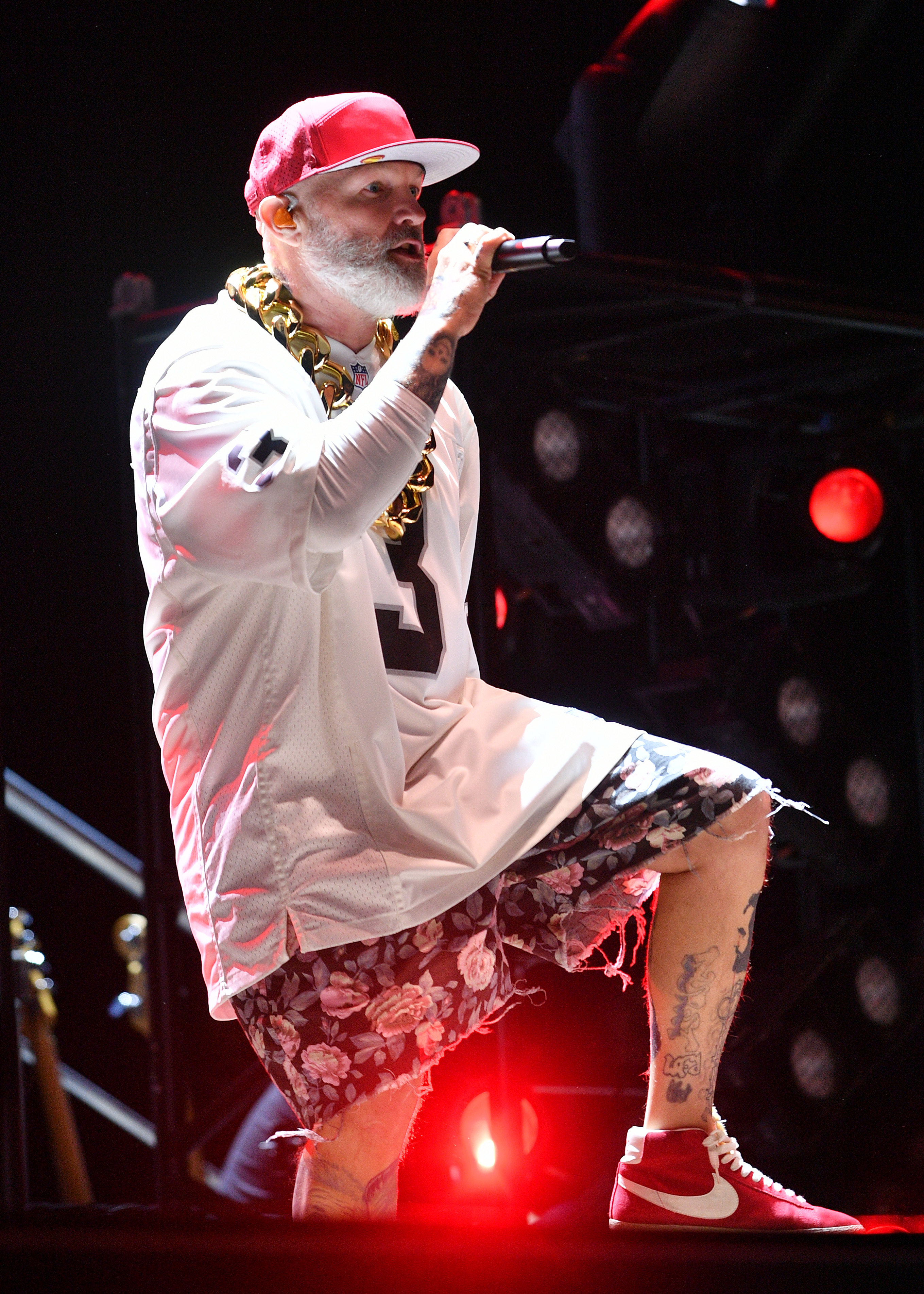 Fred Durst performs on stage, wearing a sports jersey, floral shorts, gold chain, and sneakers