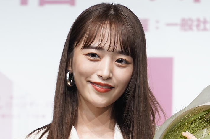 前田敦子が白いジャケットを着て、花束と賞を持っている。