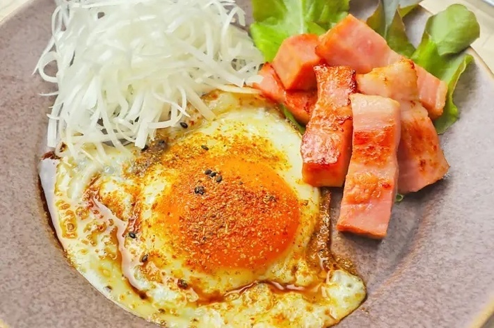 目玉焼き、ベーコン、レタスと細切り大根のサラダが乗った皿。