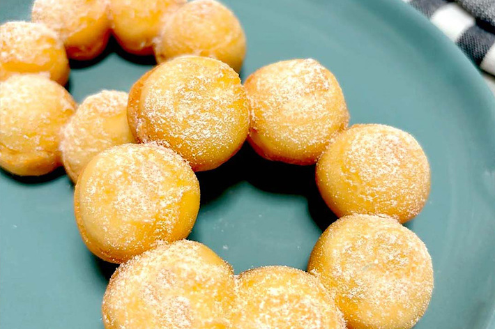 緑色の皿に揚げたボール状のドーナツが並んでいます。近くにストライプ柄の布が見えます。