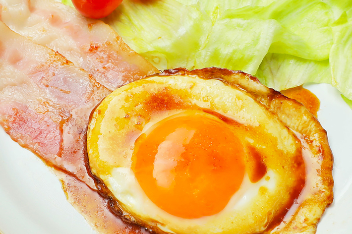 ベーコンと目玉焼き、レタスとチェリートマトが皿に盛られている朝食。