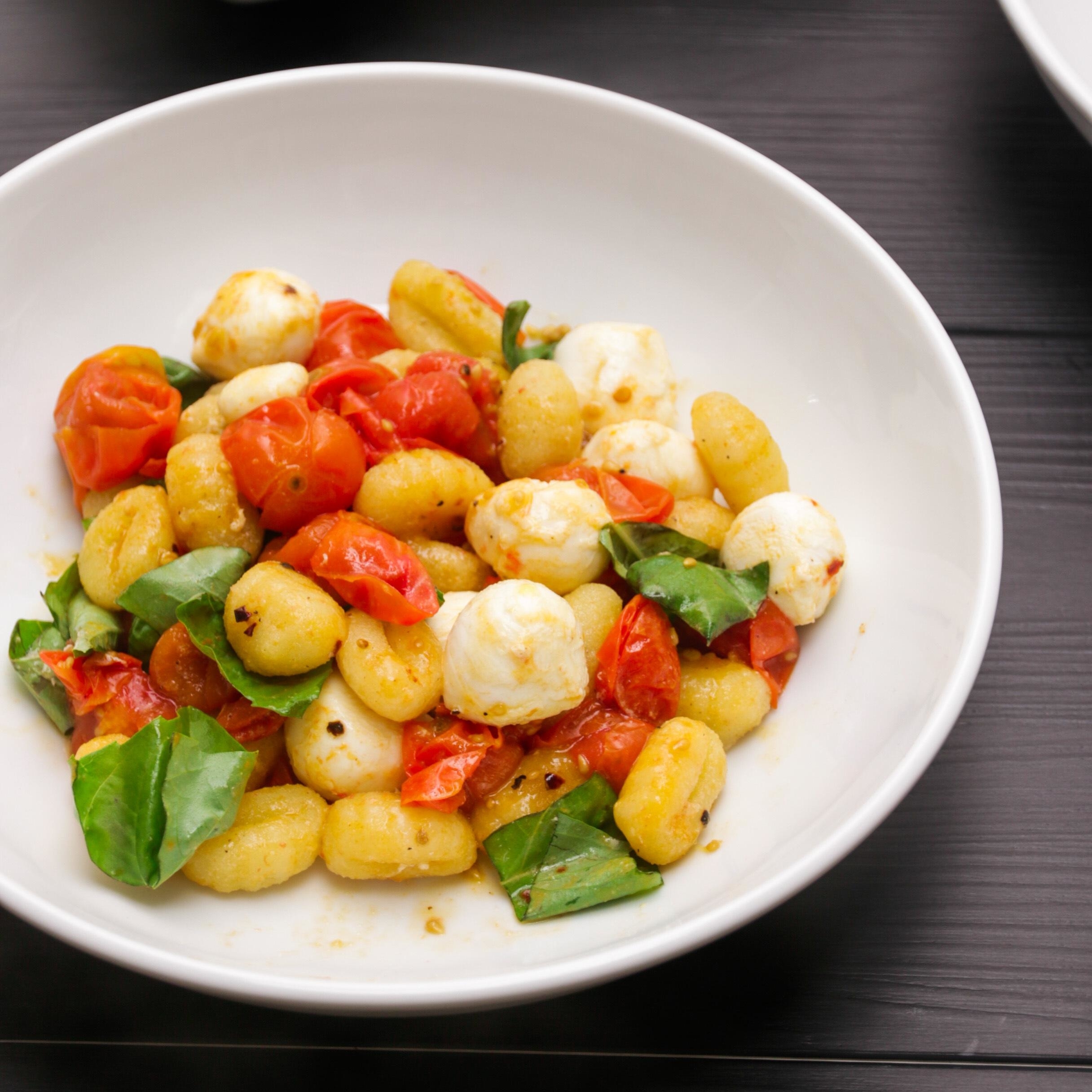A bowl of gnocchi with roasted cherry tomatoes, mozzarella balls, and fresh basil