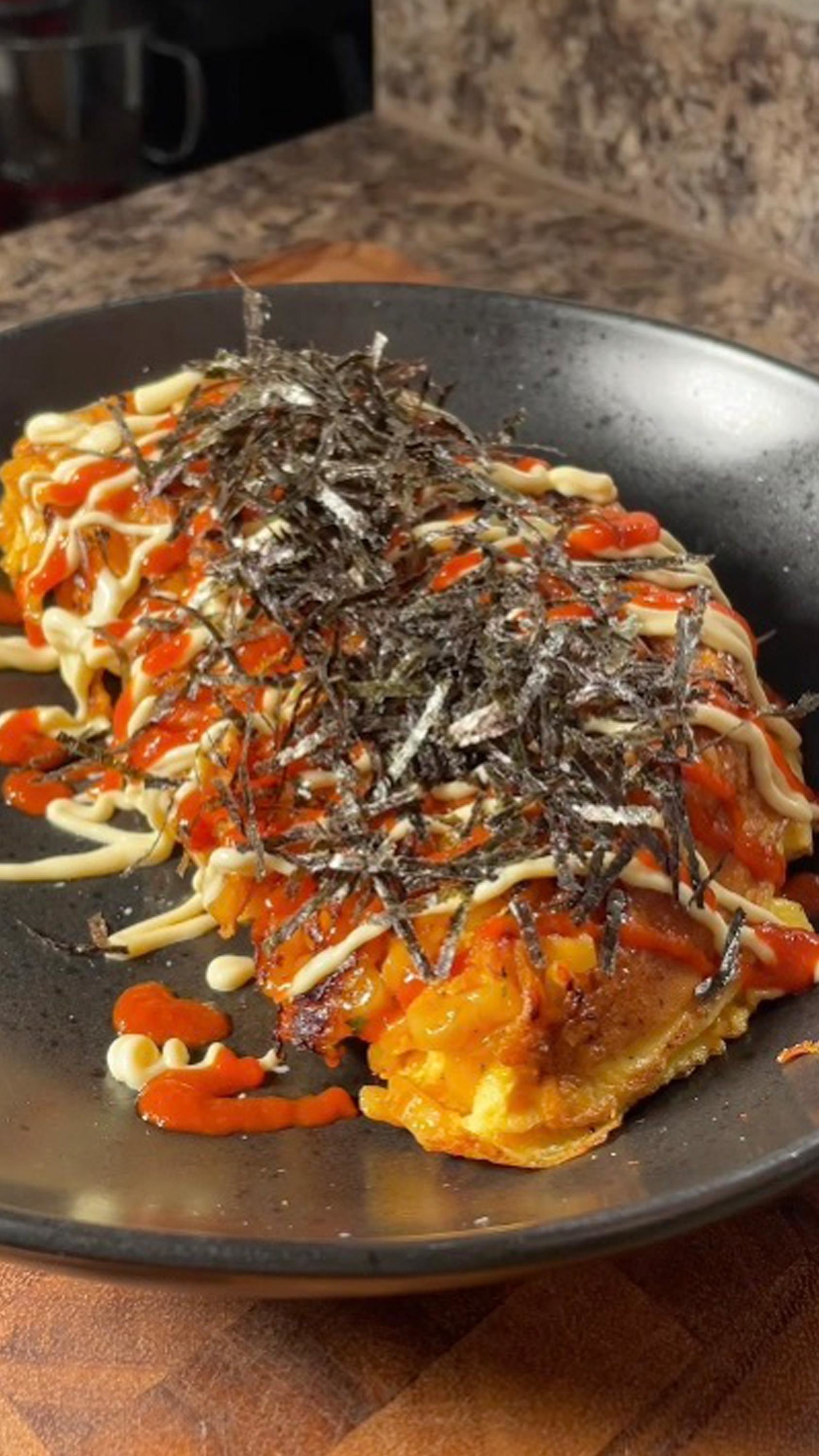 A plate of cheesy kimchi pancakes garnished with drizzled sauces and shredded nori