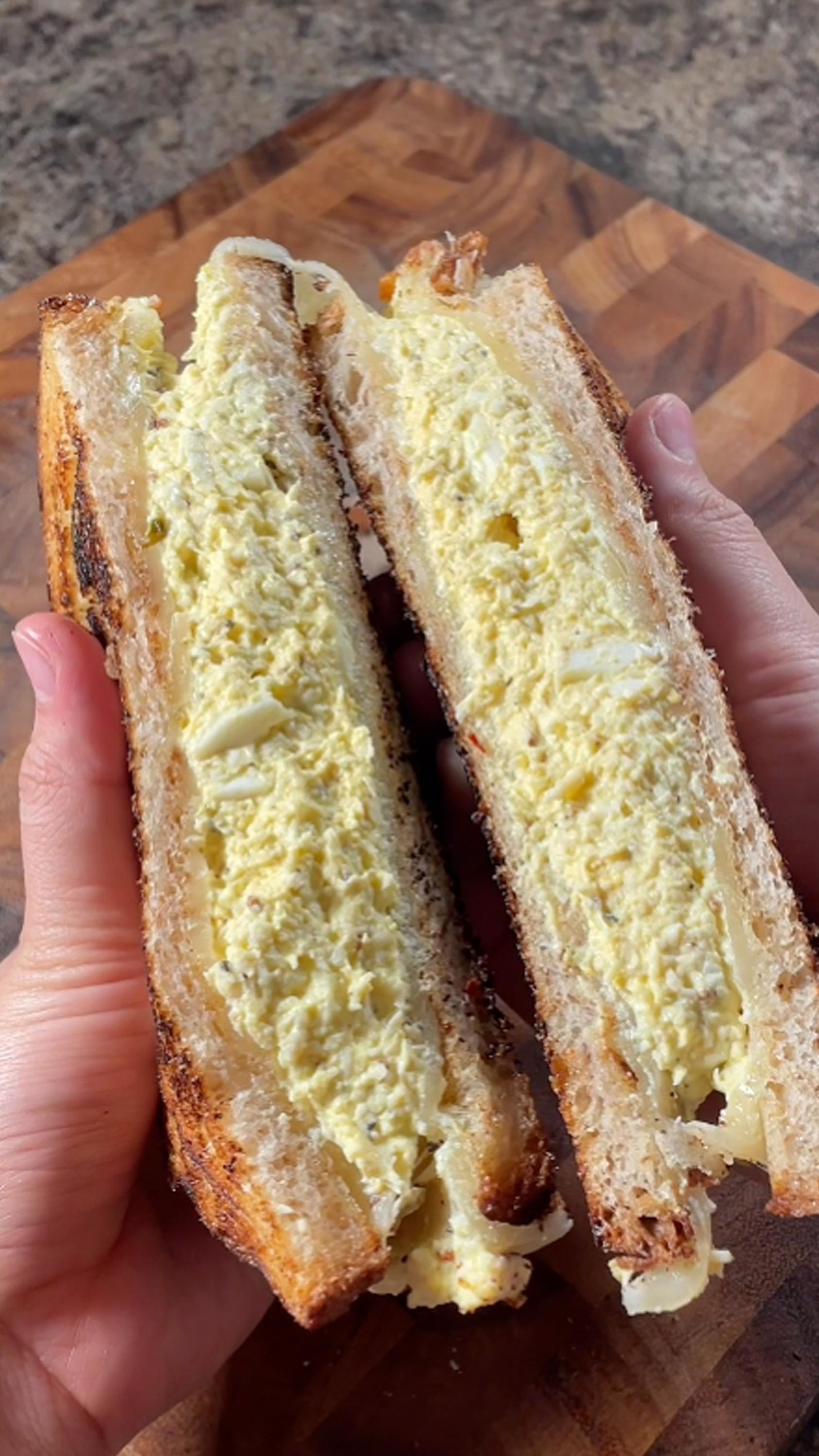 Hands holding a halved sandwich filled with a creamy egg salad