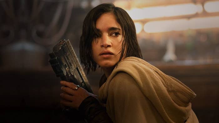 Adria Arjona as Arra Syll, holding a device and wearing a hooded cloak in a scene from the TV series "Andor."
