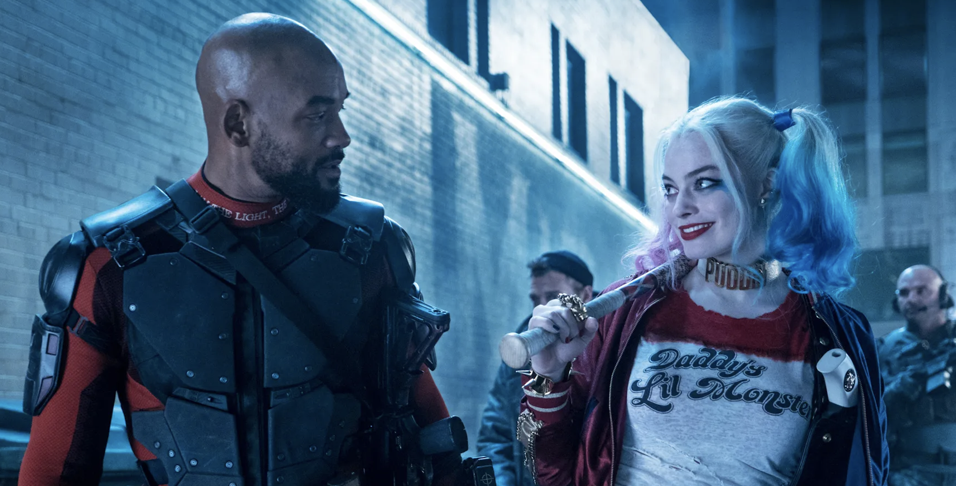 Will Smith, in combat armor, and Margot Robbie, as Harley Quinn with pigtails and a "Daddy's Lil' Monster" shirt, share a scene in a narrow alley