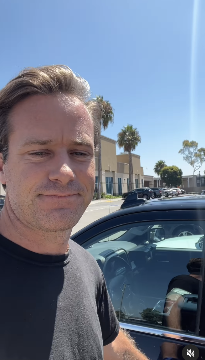 Armie Hammer takes a selfie outside with a parked car behind him