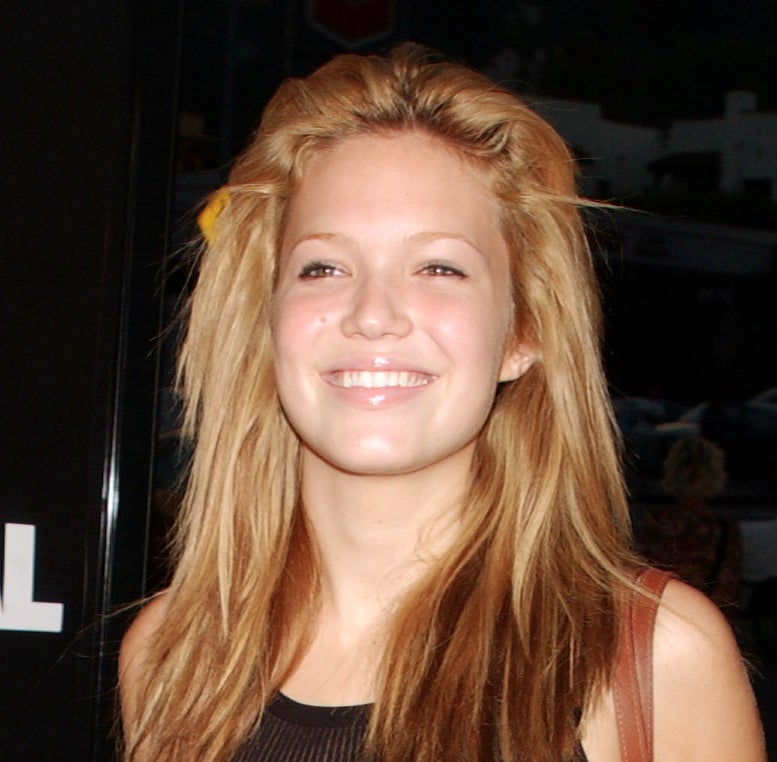 Mandy Moore walks on the red carpet, wearing a sleeveless top, long hair down, one eyebrow noticeably darker than the other