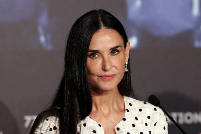 Demi Moore at a public event wearing a polka dot-patterned outfit, with long straight hair, and diamond drop earrings