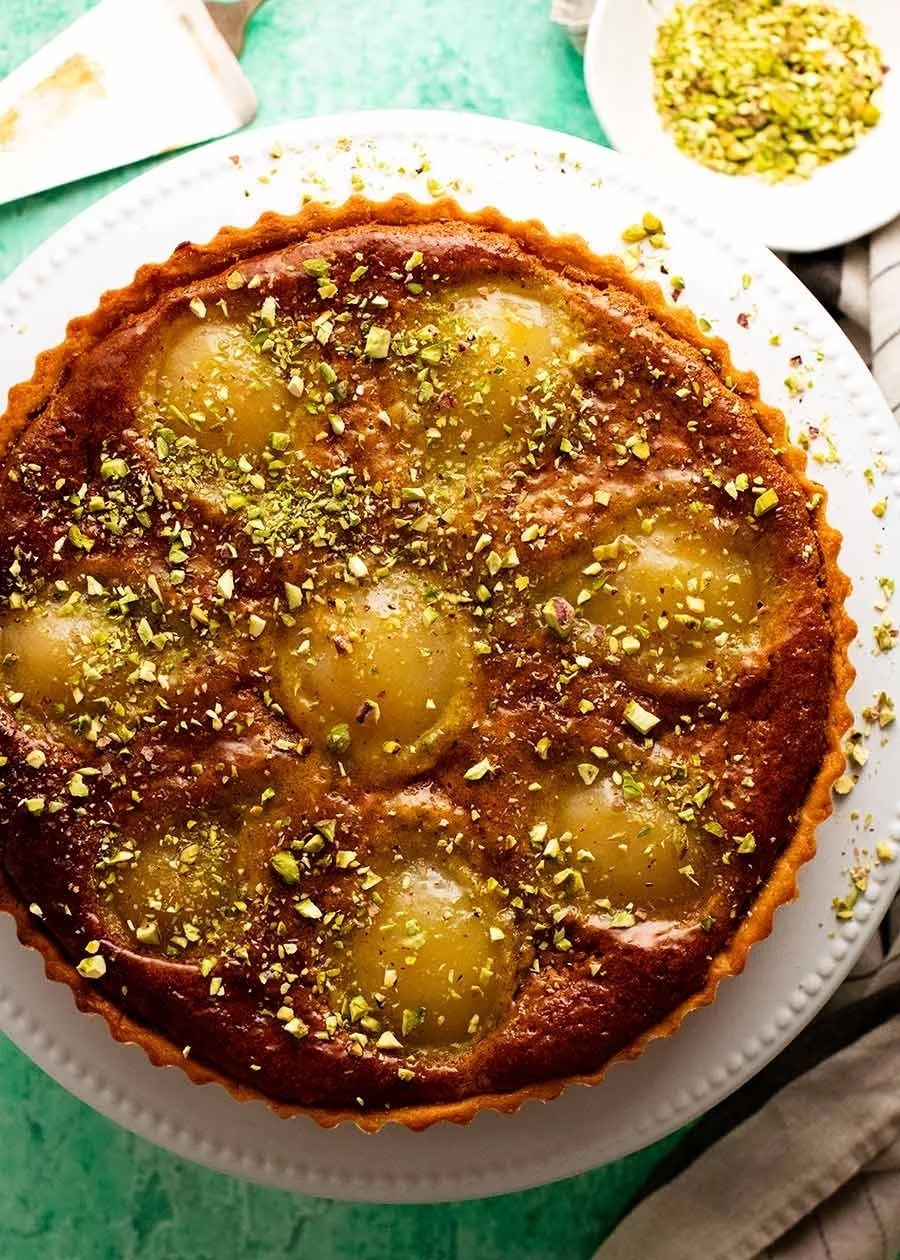 A freshly baked tart with whole pear halves and a sprinkle of chopped pistachios on top, displayed on a plate