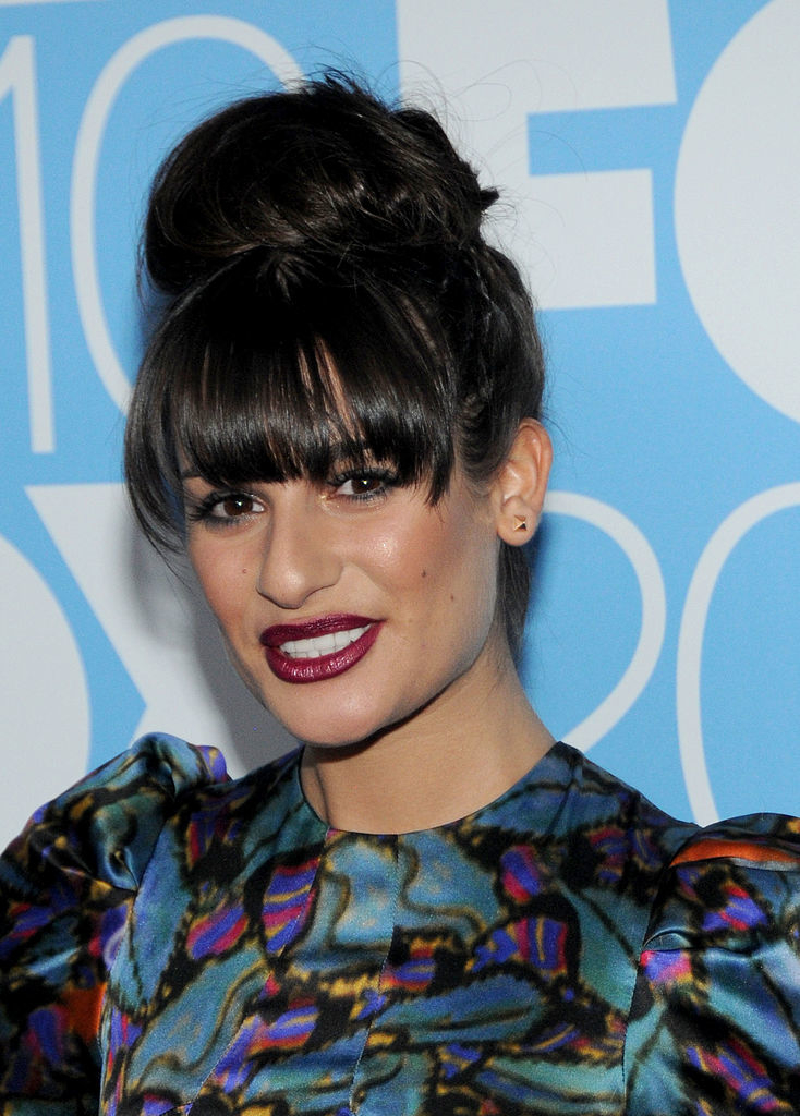 Lea Michele at a formal event, wearing a stylish patterned dress with bold sleeves and her hair in a large bun with bangs