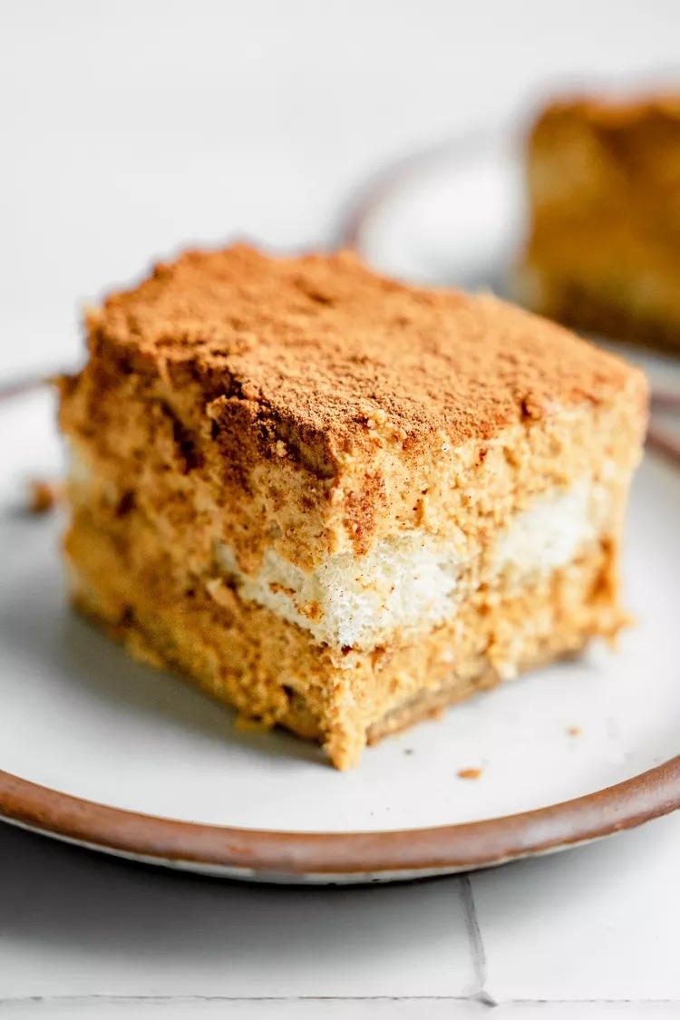 A slice of layered tiramisu with a dusting of cinnamon on a plate.