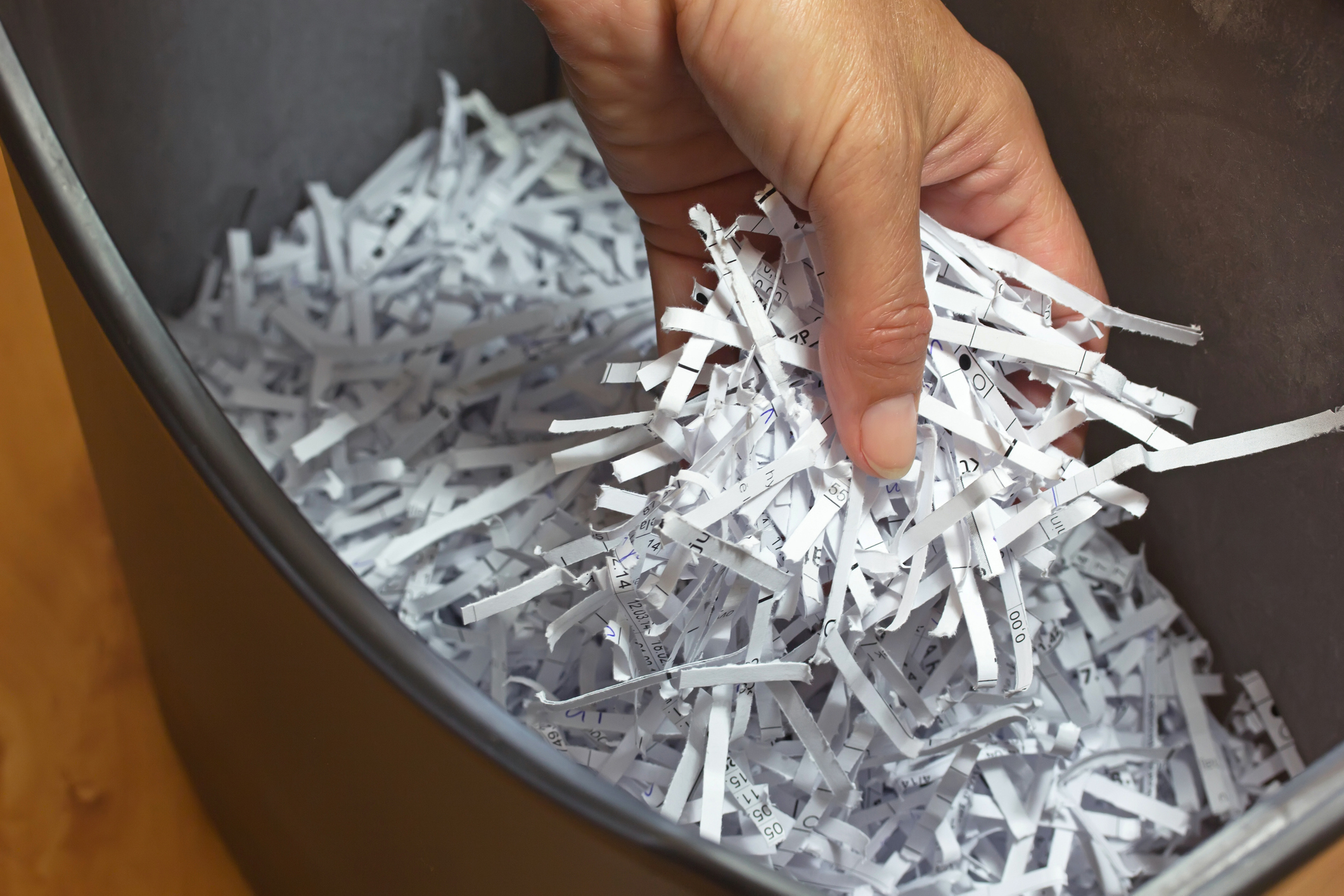 A hand is reaching into a bin filled with shredded paper
