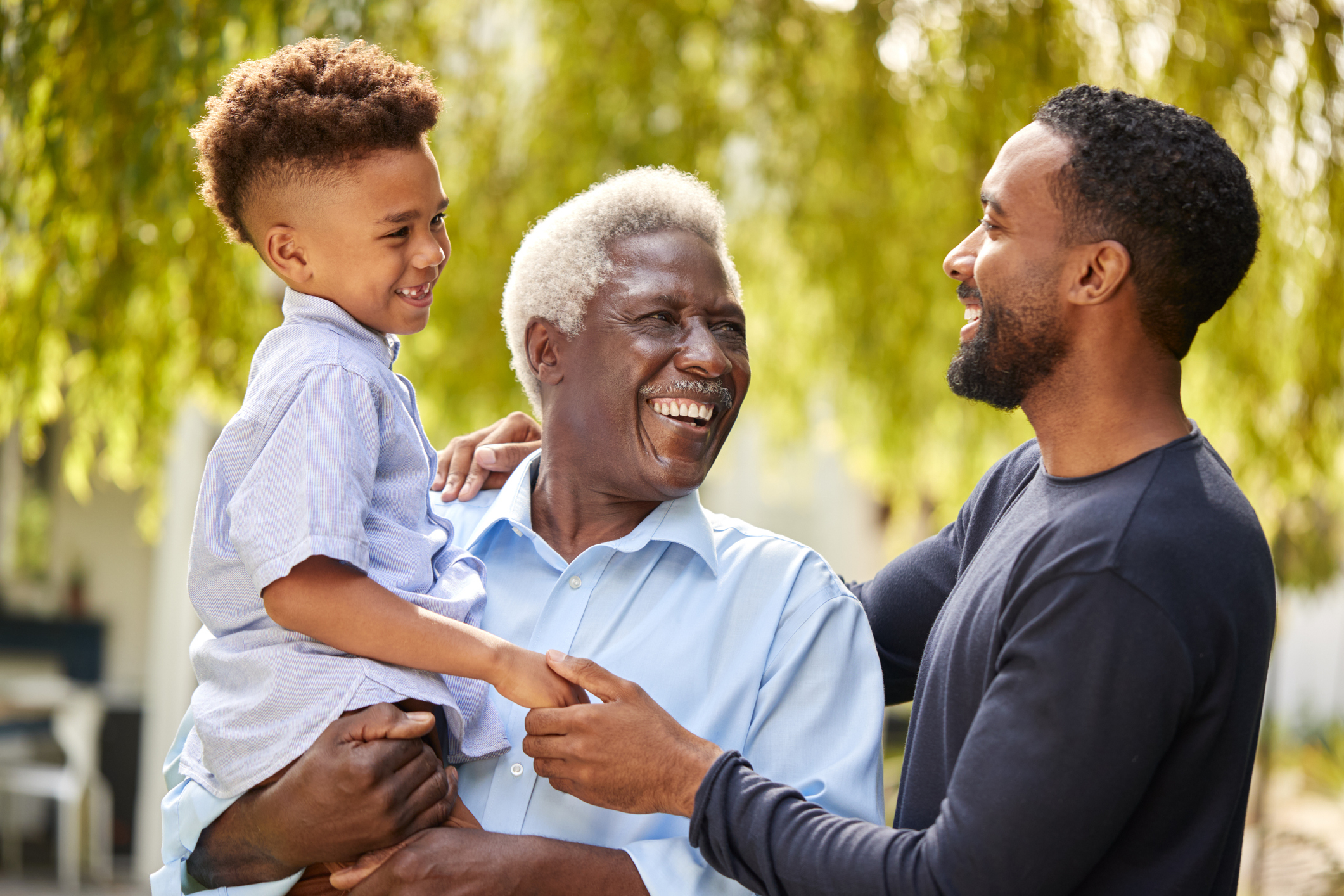 Three generations: A grandfather, father, and young boy share a joyful moment outdoors, smiling and laughing together