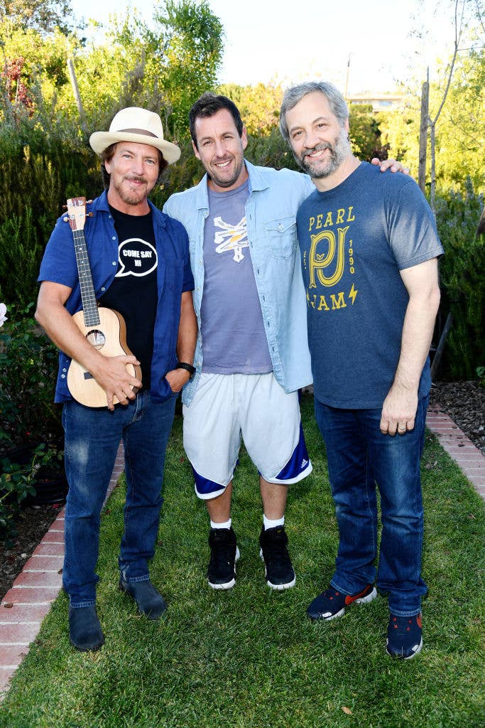 Eddie Vedder, Adam Sandler, and Judd Apatow standing together outdoors, smiling. Eddie holds a small guitar. All three are casually dressed