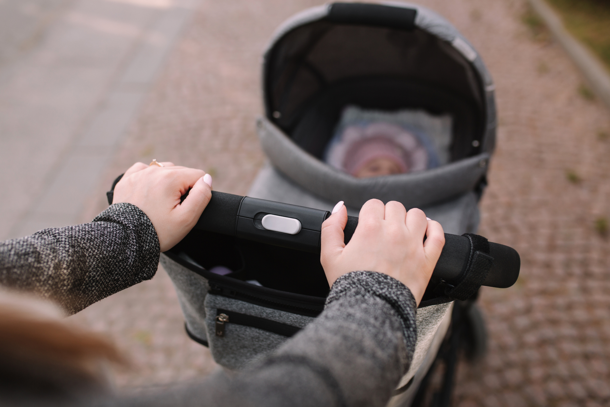 Close-up of a person pushing a baby stroller with a baby inside. The person's hands and a glimpse of the baby are visible