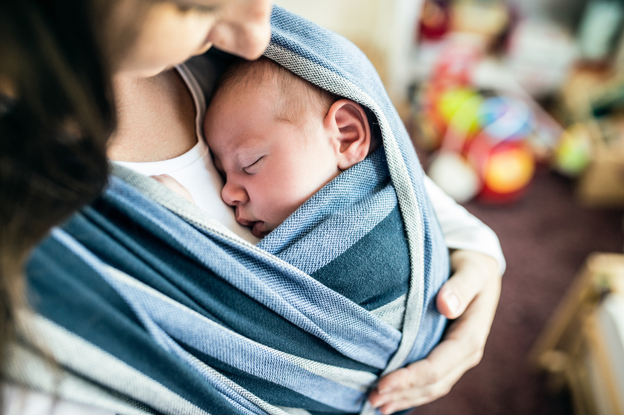 A person holds a sleeping baby wrapped snugly in a striped cloth sling
