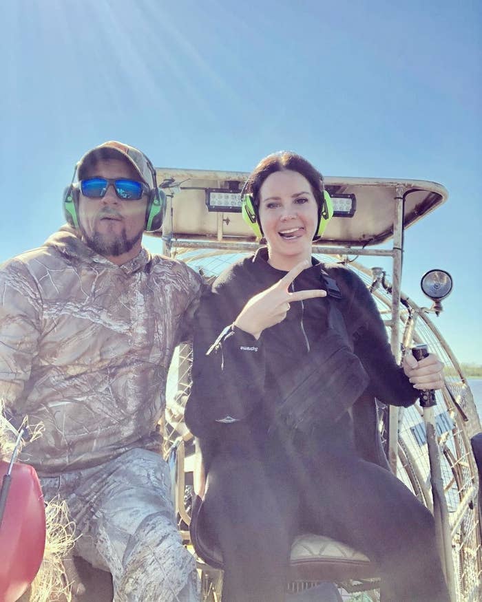 Lana Del Rey poses with Jeremy on an airboat. She shows a peace sign while both wear headsets and sunglasses