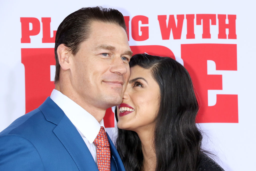 John Cena in a suit and tie smiles while holding Shay Shariatzadeh, who is looking at him affectionately at the &quot;Playing With Fire&quot; premiere