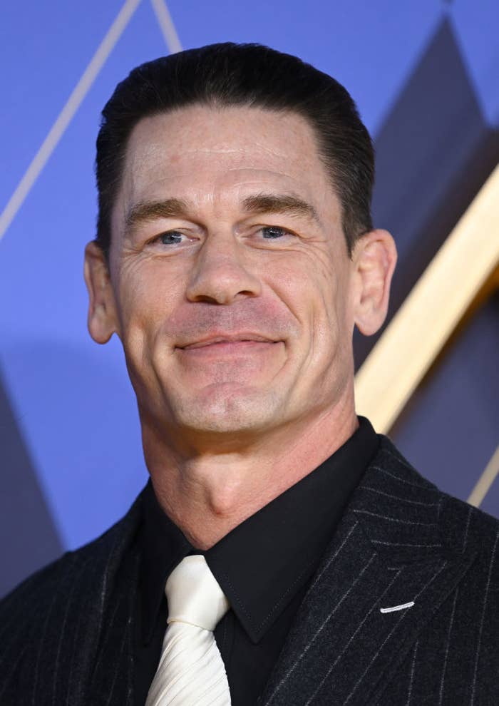 A closeup of John Cena smiling, wearing a pinstripe suit with a tie at an event