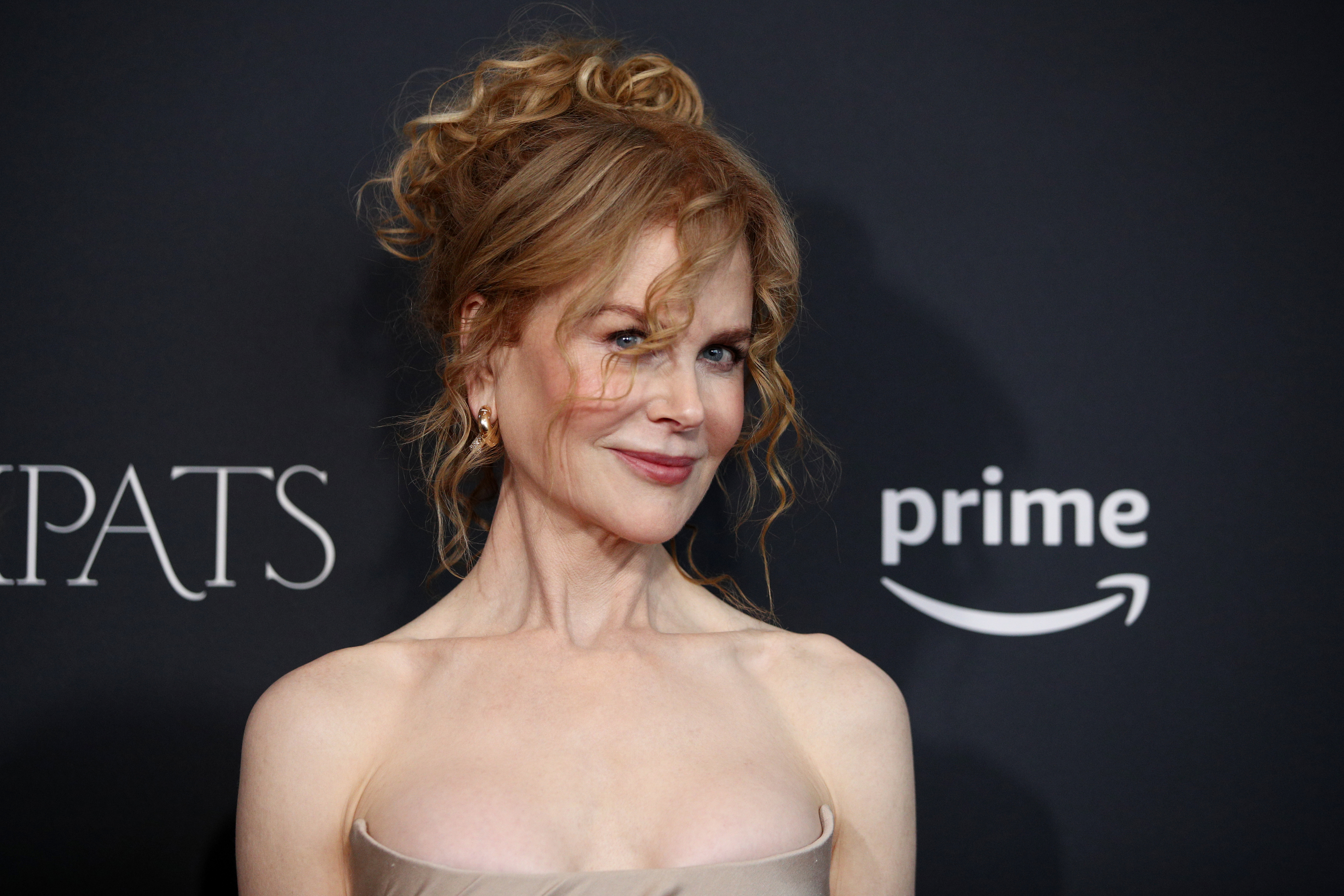 Nicole Kidman poses on the red carpet in a strapless evening gown, with a wavy updo hairstyle, at the event for the TV series "Expats"