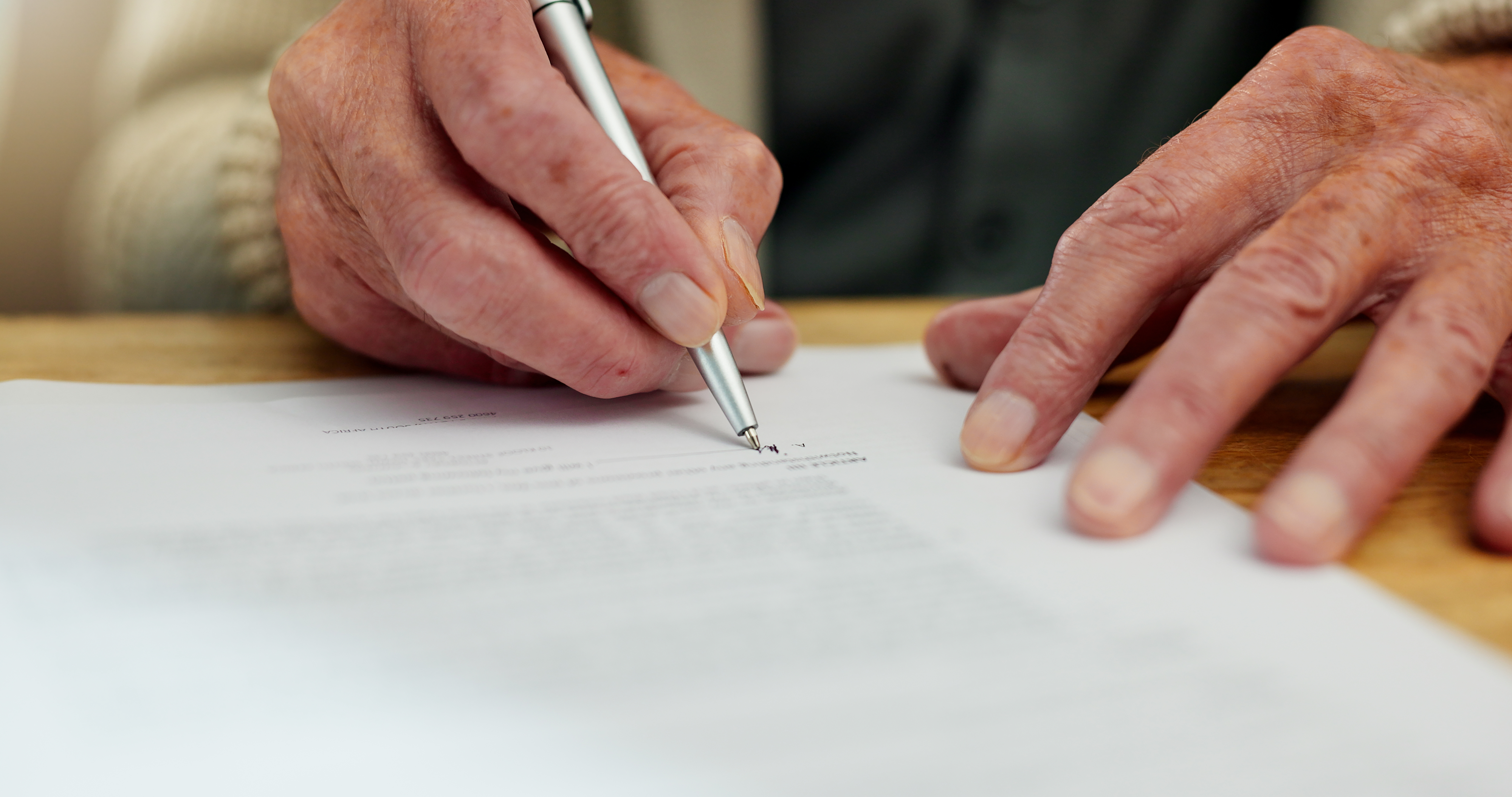 An elderly person signing a document with a pen