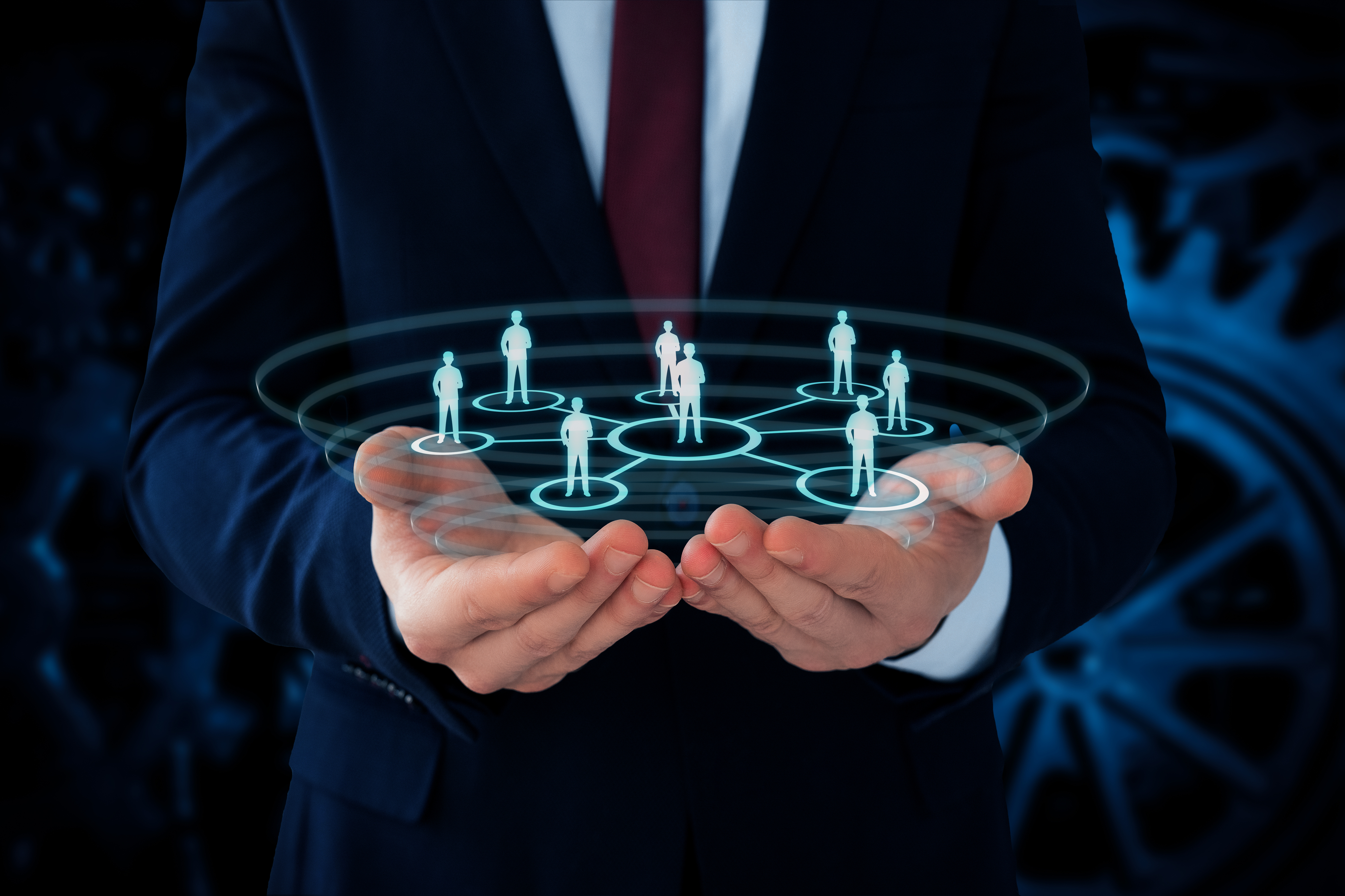 A businessman's hands hold a 3D digital network with holographic human figures connected in a circular pattern, symbolizing teamwork and connectivity