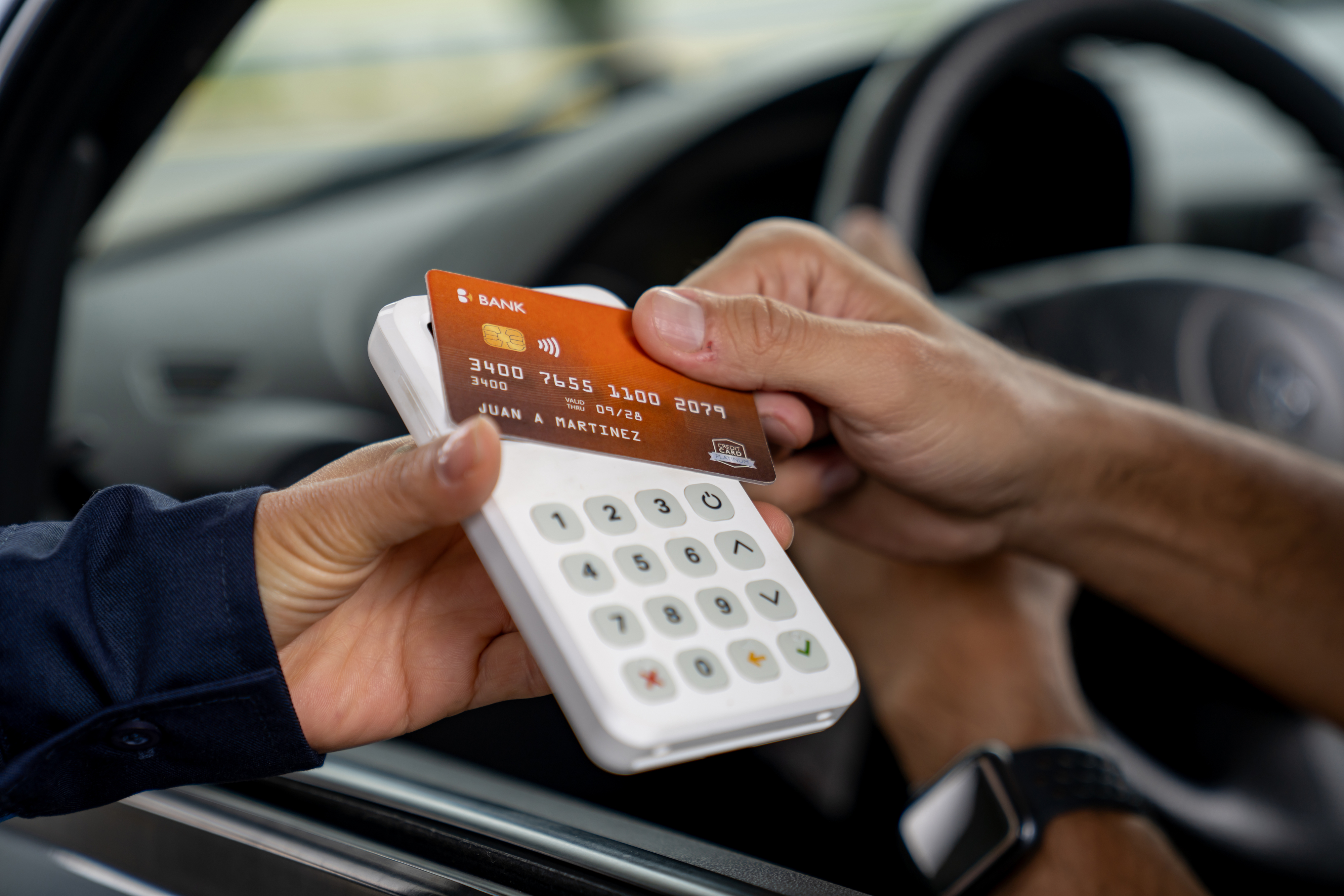 A person is using a credit card at a mobile card reader held by another individual, possibly for a transaction from a vehicle