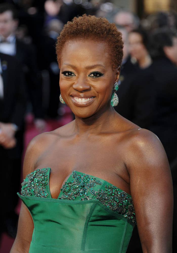 Viola Davis smiles while wearing an elegant strapless dress adorned with intricate detailing. She also wears matching earrings
