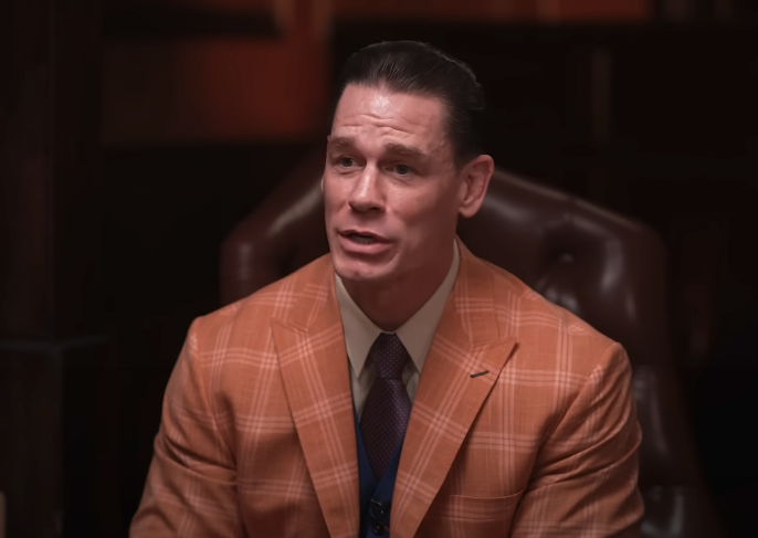 John Cena, in a checkered suit, seated and speaking during an interview