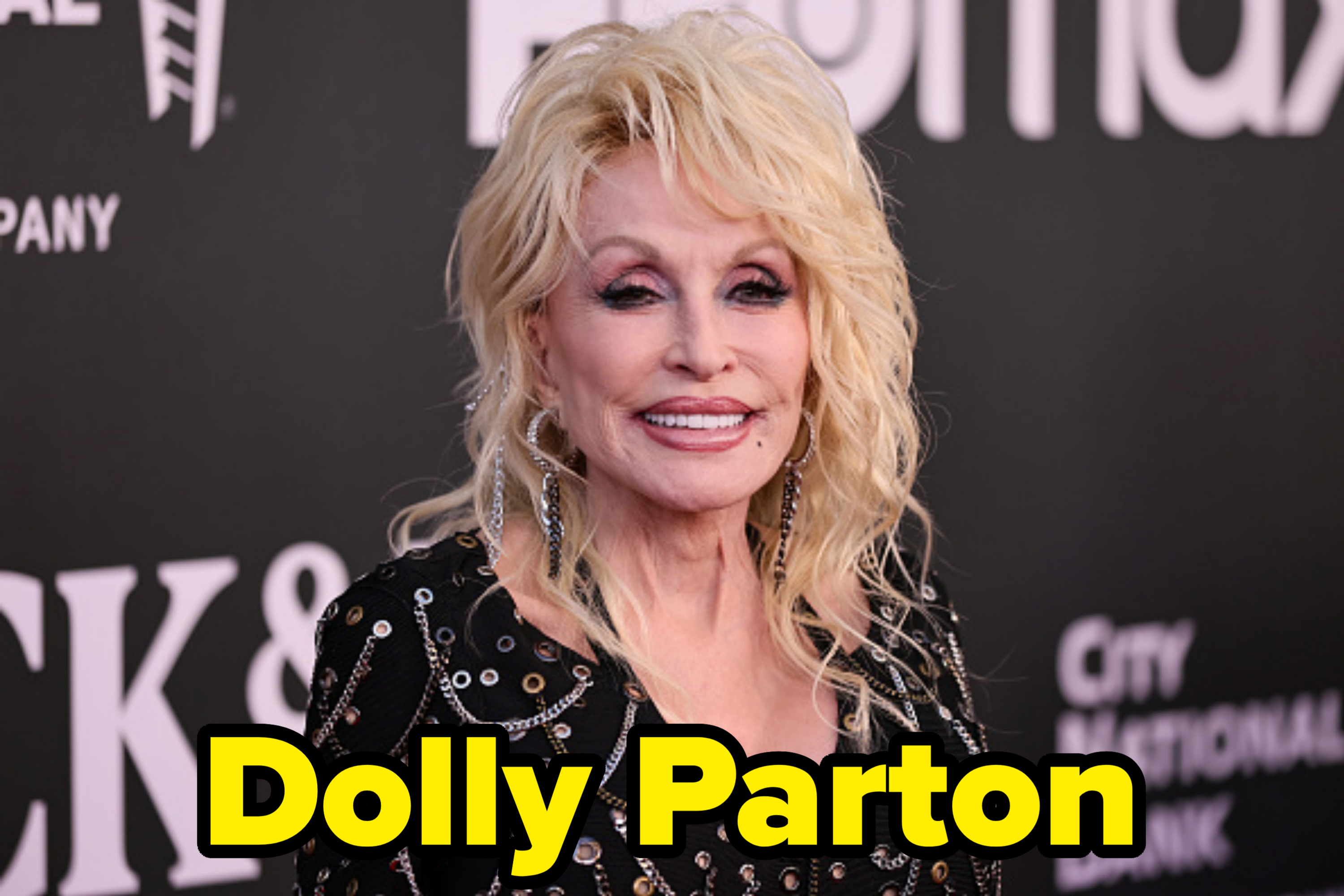 Dolly Parton at a red carpet event, wearing a black outfit adorned with metallic embellishments and dangling earrings