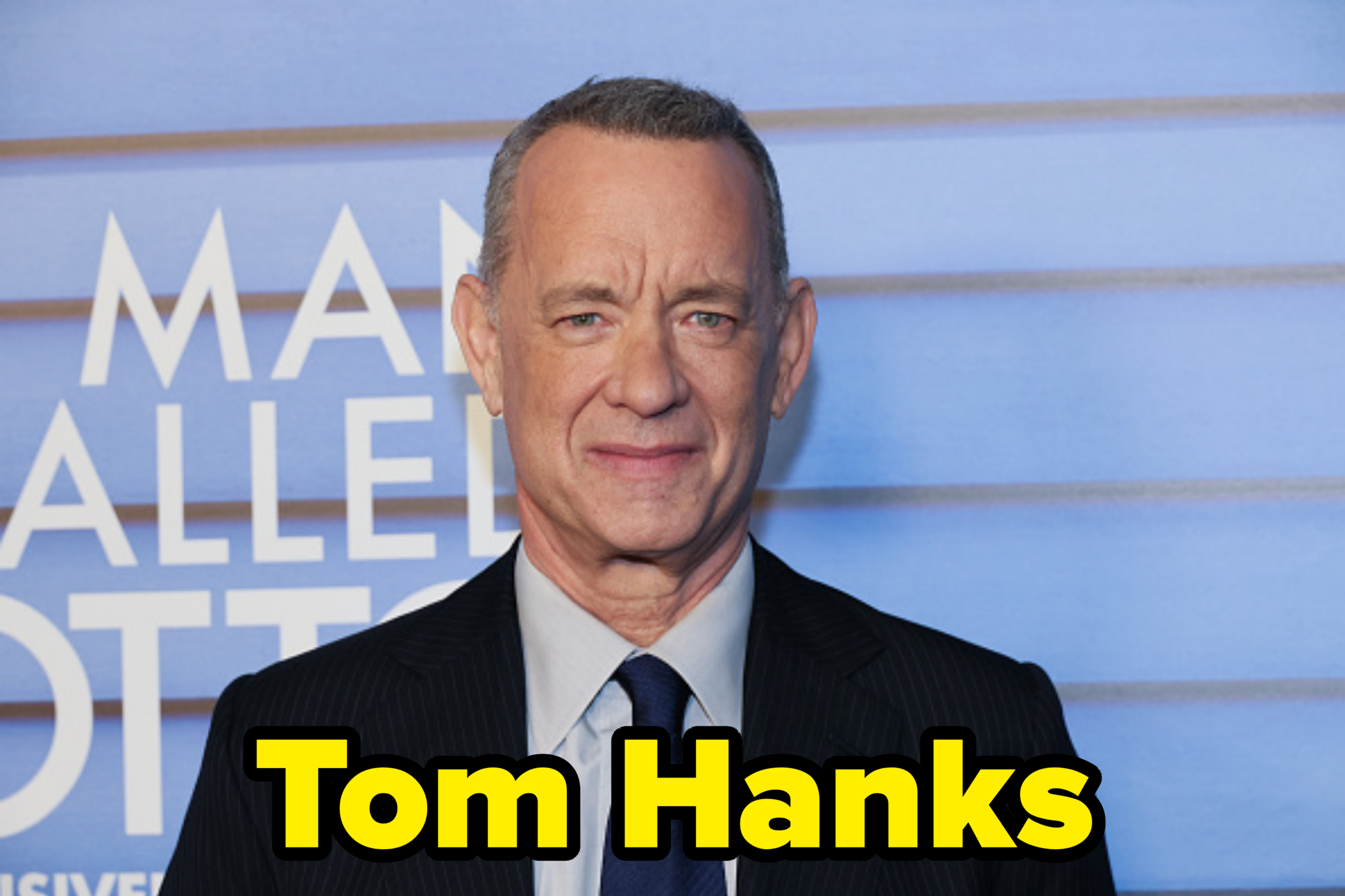 Tom Hanks, dressed in a dark suit and tie, at an event promoting &quot;A Man Called Otto.&quot; Text on the background reads &quot;A Man Called Otto.&quot;