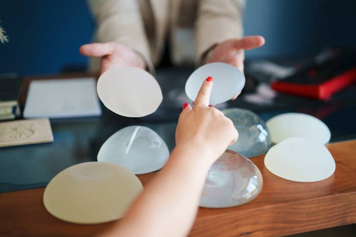 Two hands pointing and presenting different types of silicone breast implants on a table