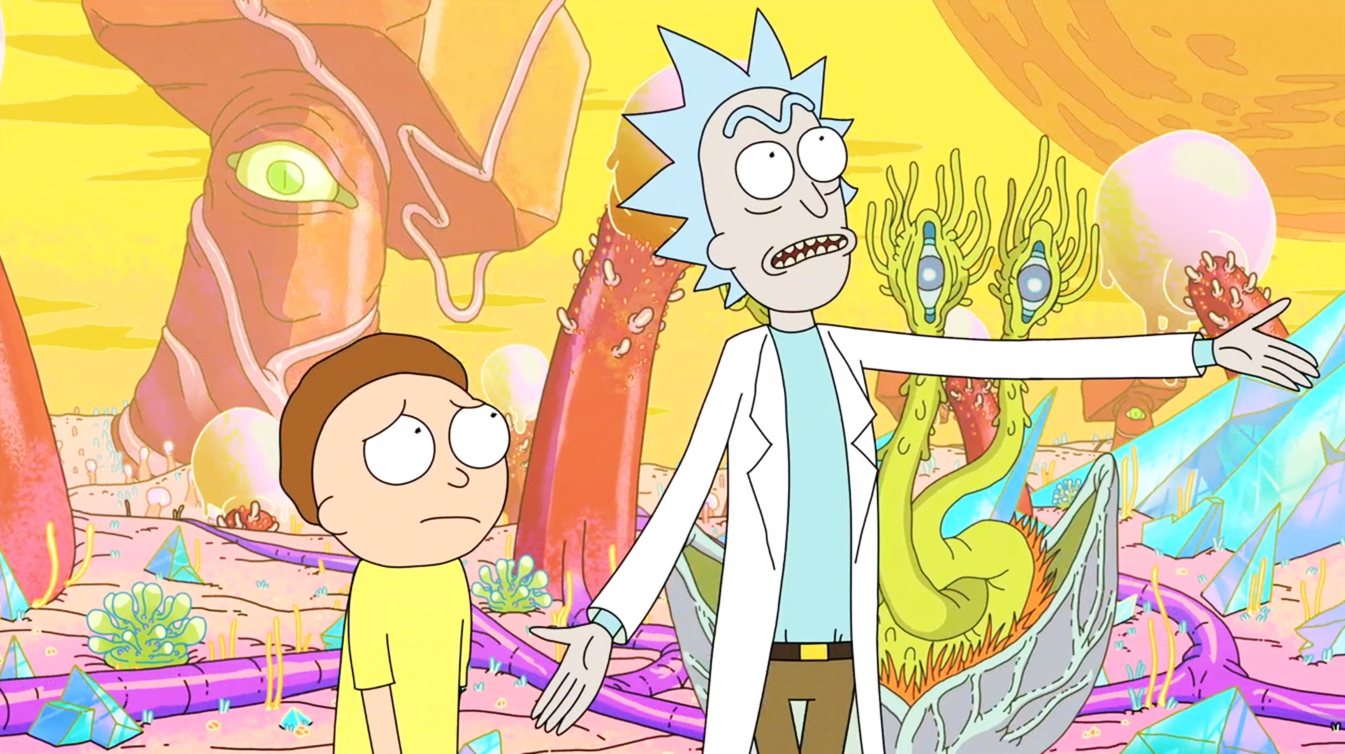 Rick and Morty stand in a colorful alien landscape. Rick appears to be explaining something while Morty looks concerned
