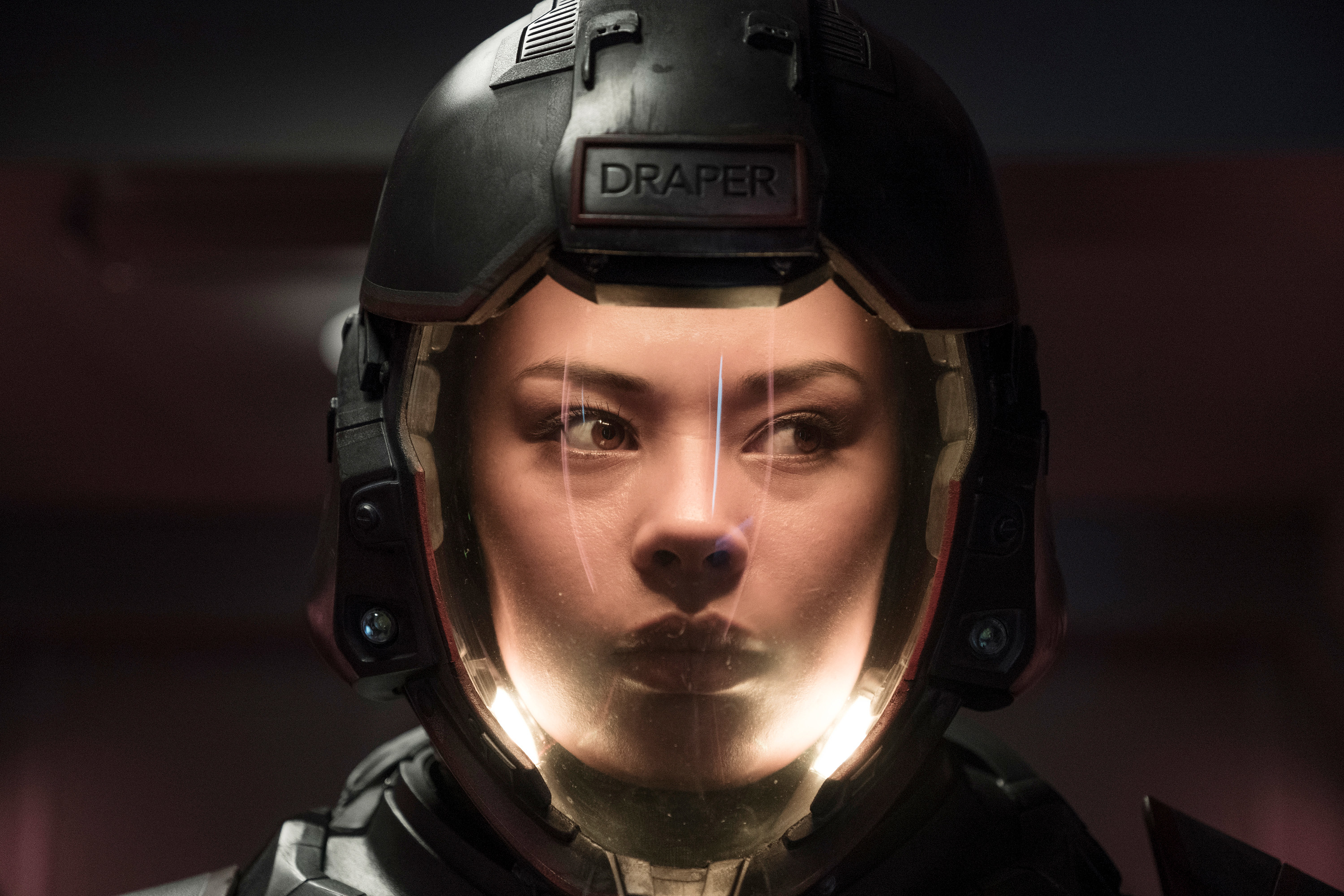 Person in futuristic armored suit and helmet labeled "DRAPER," face visible through helmet visor
