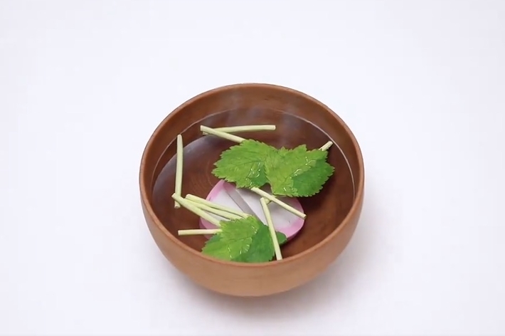 木製のボウルに盛られた料理。細く切った野菜と葉が見える。