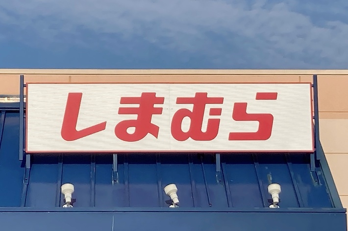 Storefront with a sign in Japanese characters, reading “Shimamura,” above the entrance. A blue accessibility sign is visible in front of the store