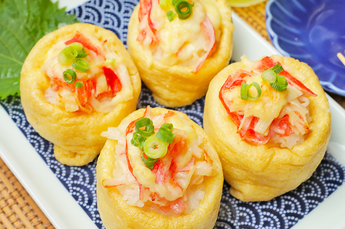 四つの海老入りいなり寿司が白い皿に並んで置かれています。上には刻んだネギがトッピングされています。