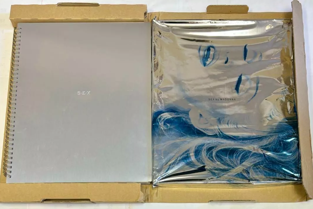 "Sex by Madonna" book cover in packaging, featuring a spiral-bound silver notebook and a foil-wrapped book with a blue photo of Madonna's face