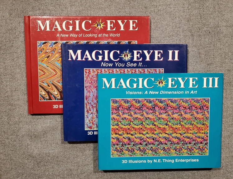 Three Magic Eye books titled, from front to back: "Magic Eye III: Visions: A New Dimension in Art," "Magic Eye II," and "Magic Eye: A New Way of Looking at the World."