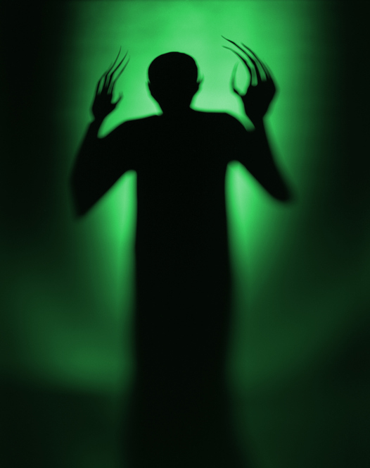 Silhouette of a person with exaggeratedly long fingers against a green background, hands raised near the head in a dramatic pose