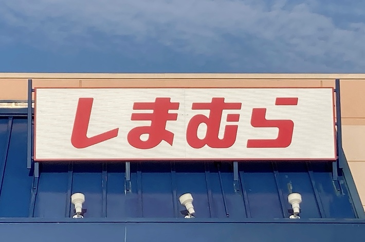A storefront with a sign displaying large Japanese characters. The store accessibility features include a visible handicap parking sign in the foreground