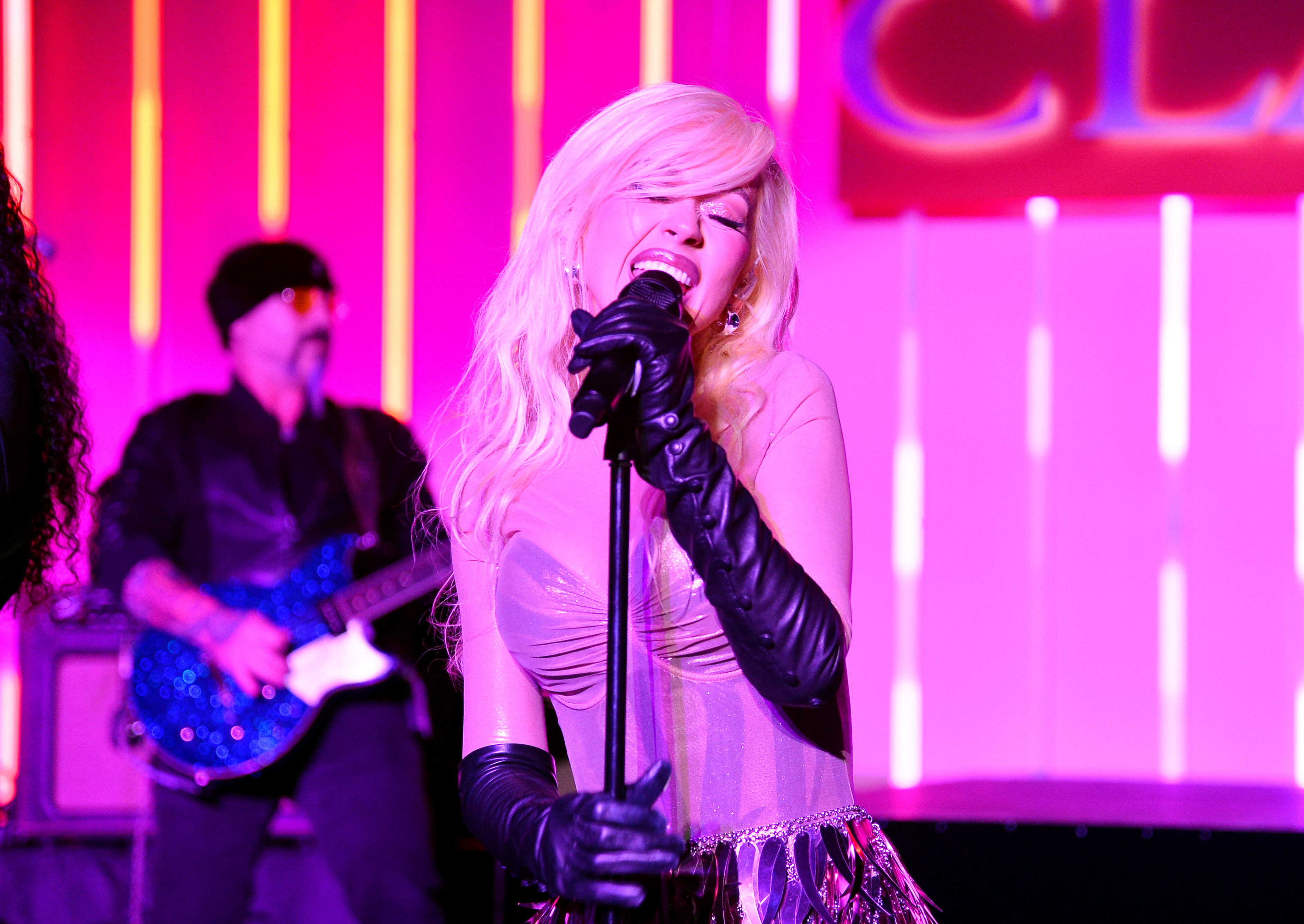 Christina Aguilera performs passionately on stage in a glamorous outfit, accompanied by a guitarist in the background
