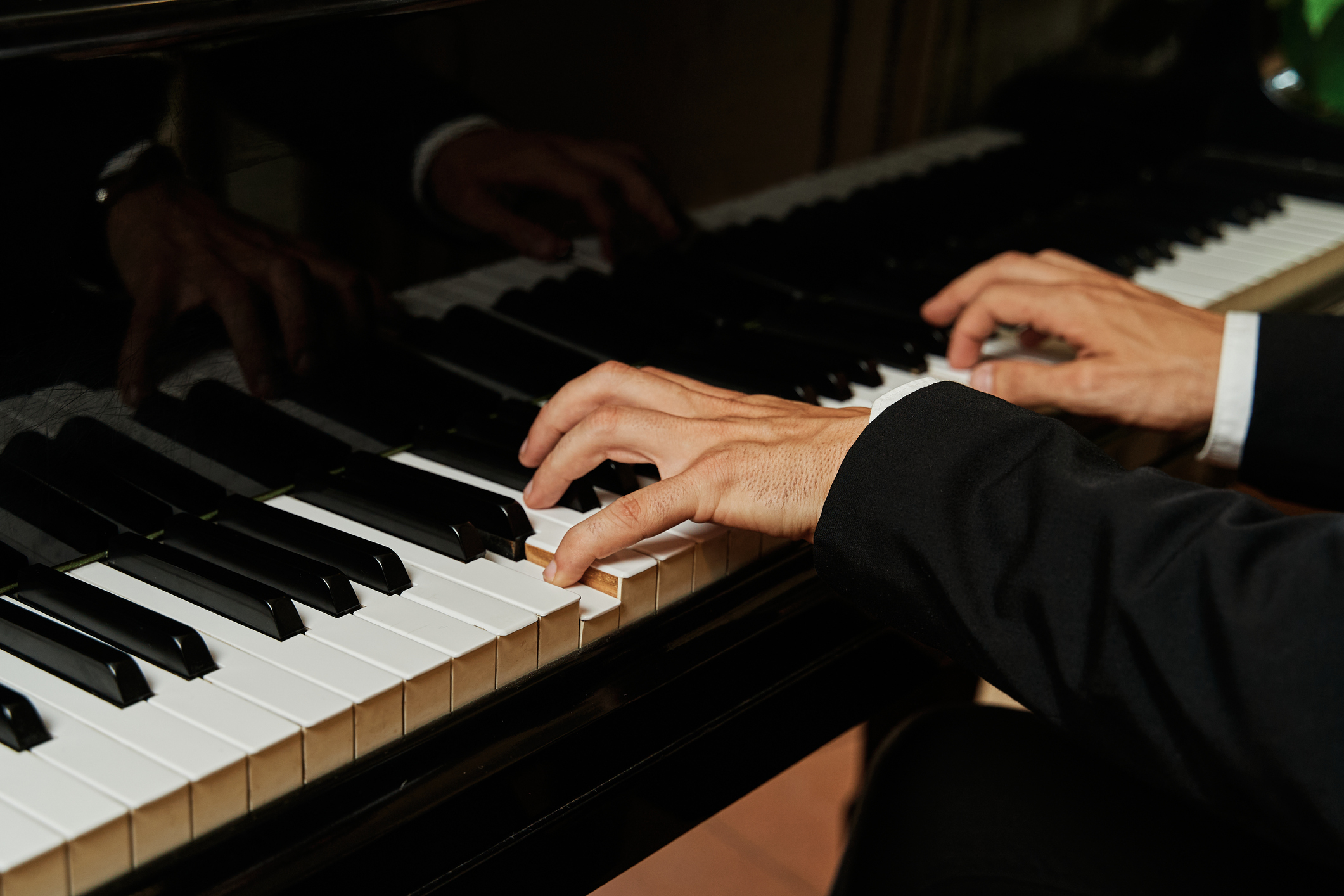 Close-up of a person in formal attire playing a grand piano, highlighting their hands and the piano keys