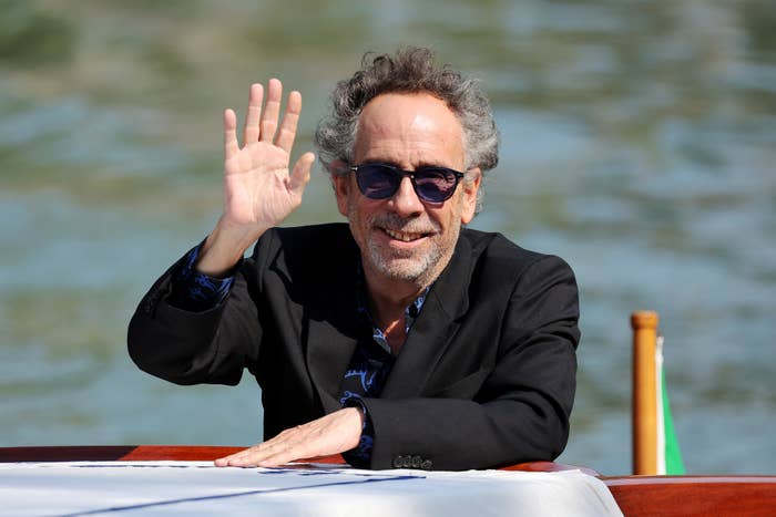 Man with curly hair and sunglasses waves while leaning on a boat railing