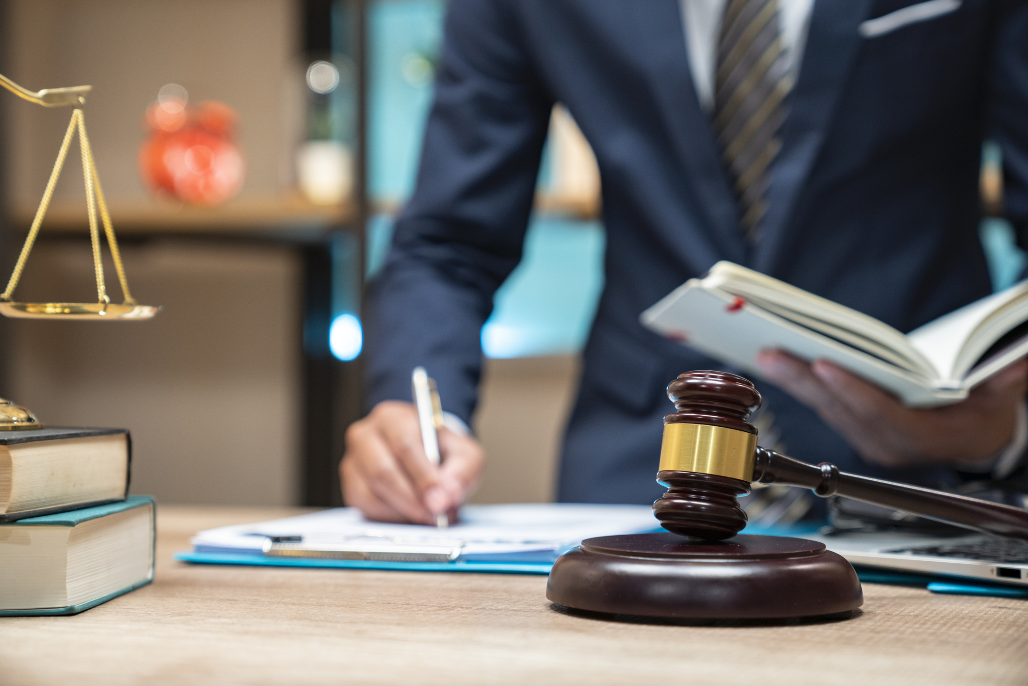 A person in a suit stands at a desk with legal documents, a gavel, and scales of justice, symbolizing legal work and decision-making in a professional environment