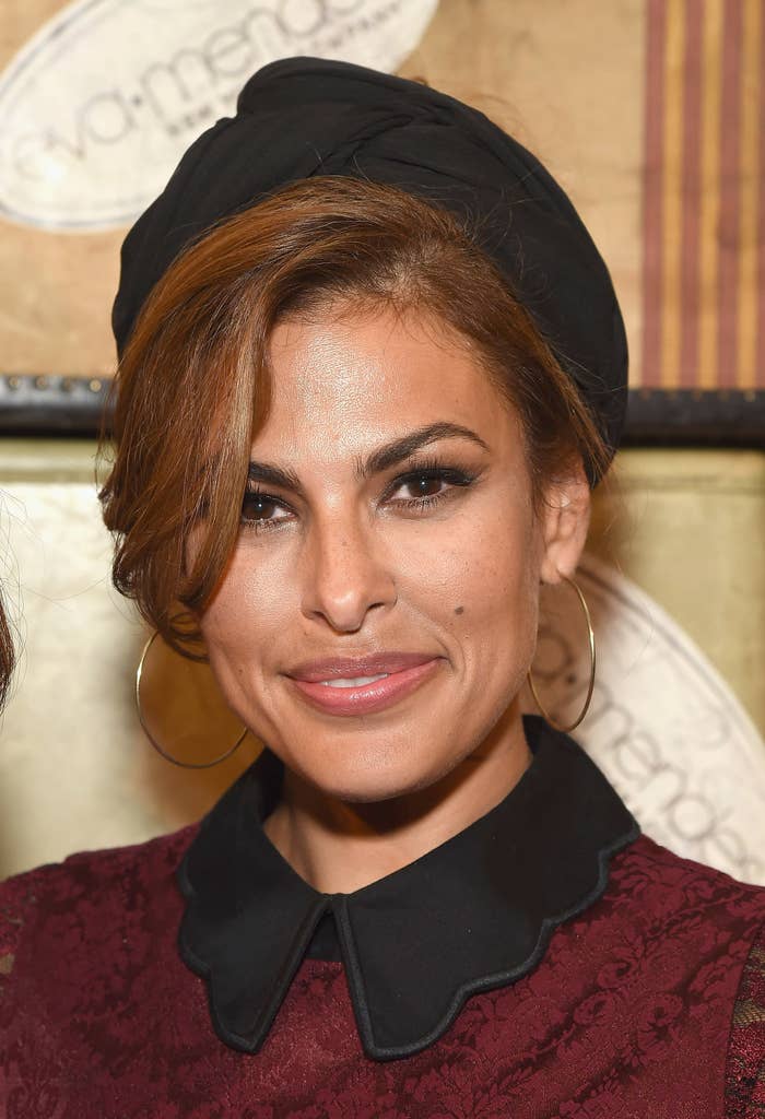 Eva Mendes smiles while wearing a hair wrap, hoop earrings, and a dress with a scalloped collar