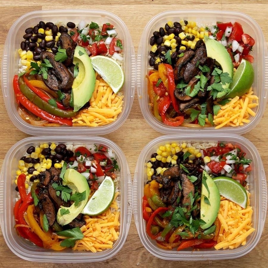 Four meal prep containers filled with rice, black beans, corn, bell peppers, avocado slices, lime wedges, grated cheese, and topped with cilantro
