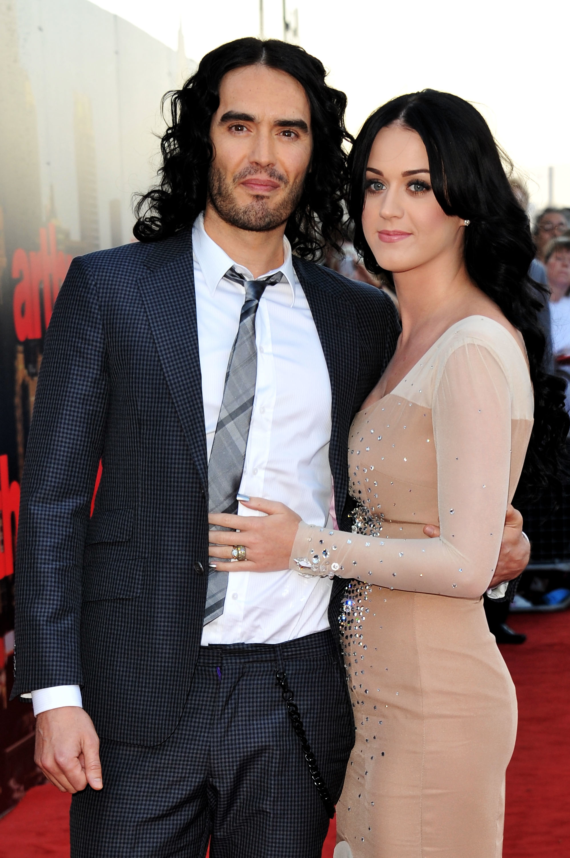 Russell Brand and Katy Perry standing together on the red carpet. Russell is in a suit and tie, while Katy is in a form-fitting dress
