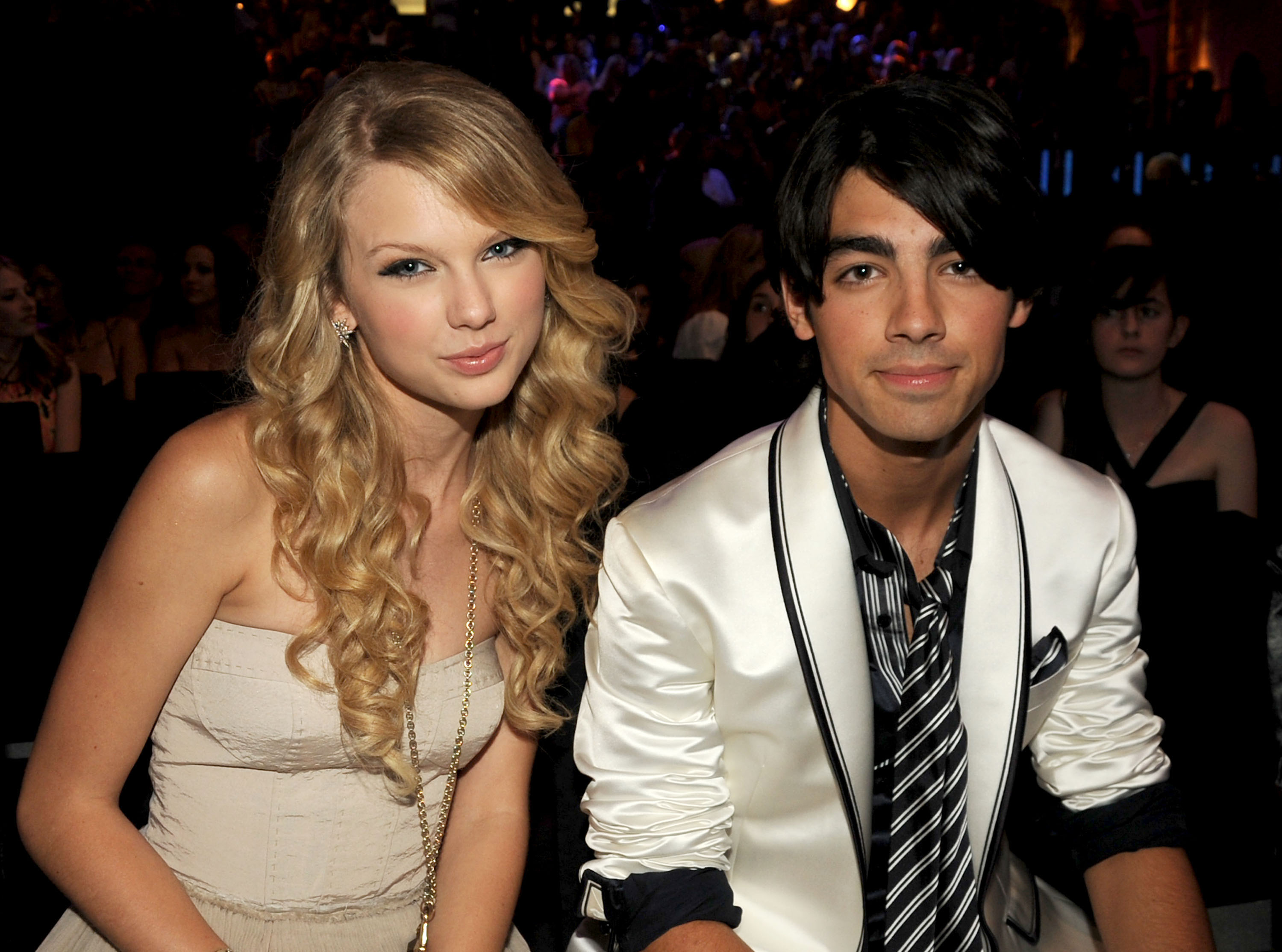 Taylor Swift and Joe Jonas at a formal event, Swift in a strapless dress and Jonas in a white suit with a black shirt and striped tie